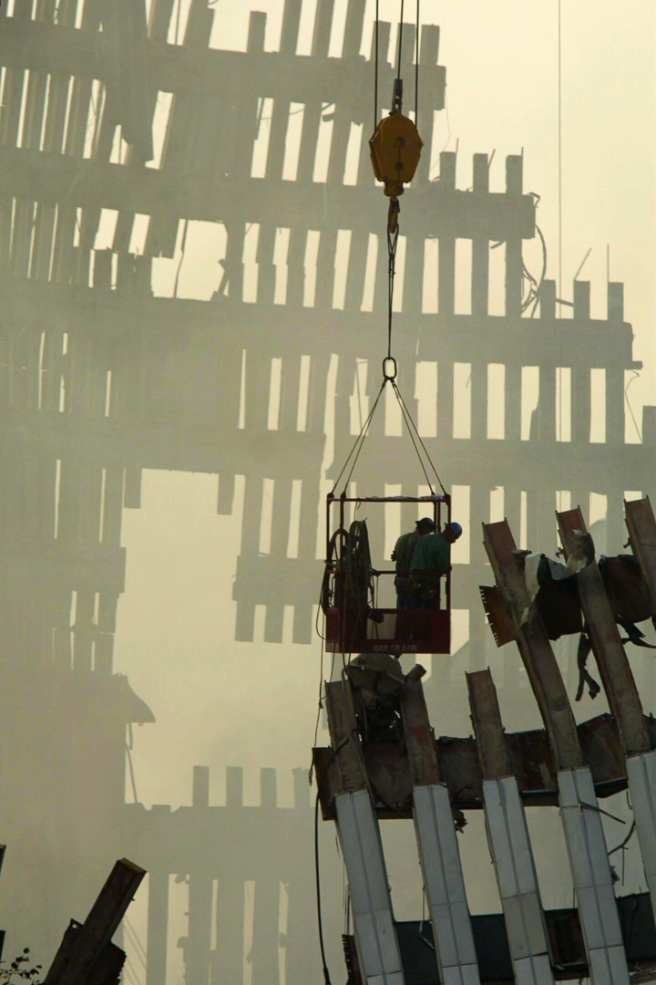 Two emergency workers inspect ruins suspended from a crane.